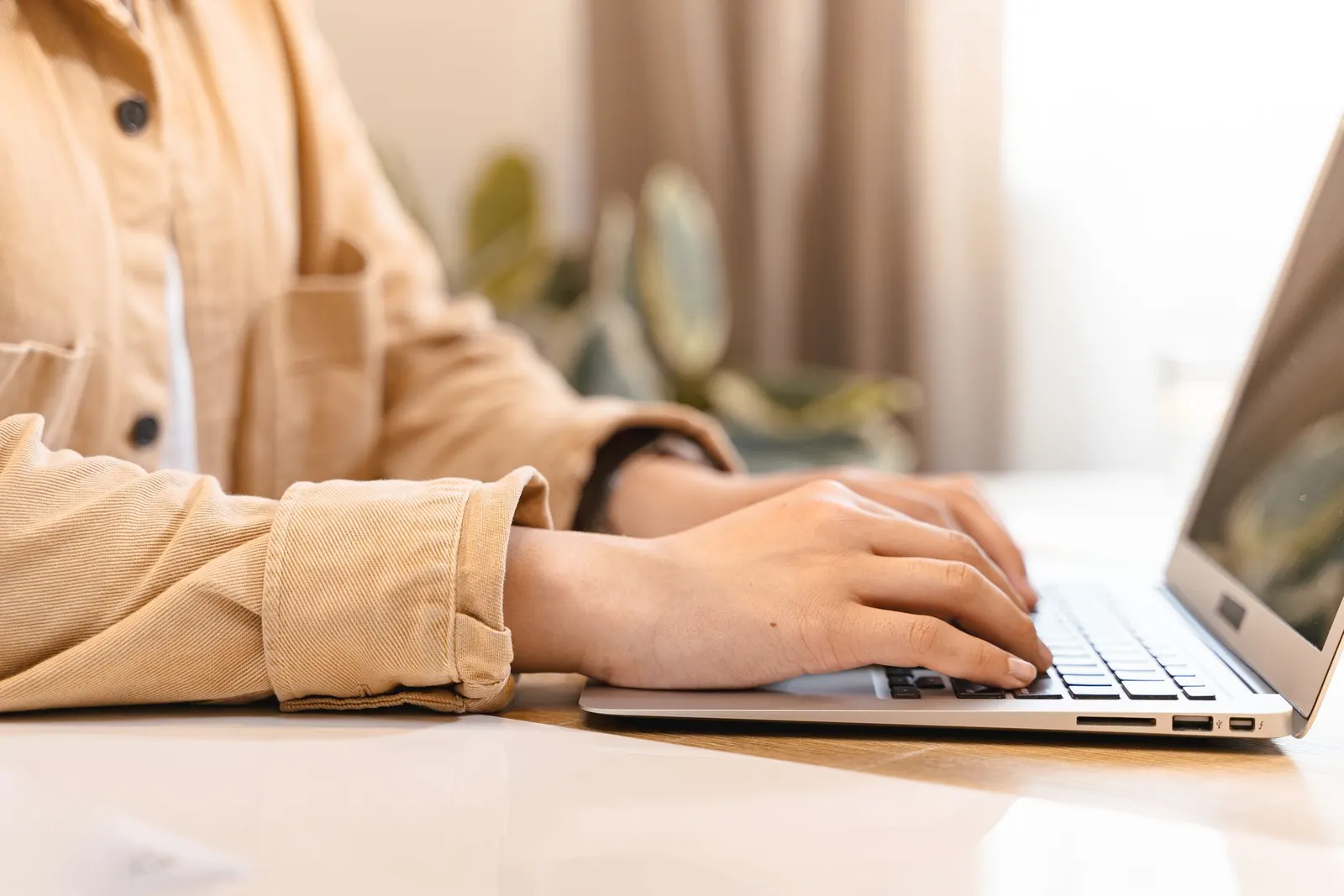 Twee handen typen op het toetsenbord van een laptop op een lichte houten tafel
