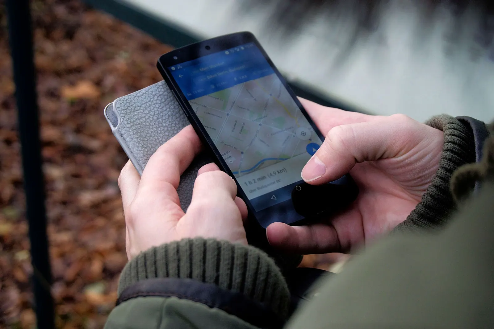 Duas mãos seguram, ao ar livre, um celular em que um app de mapas mostra um mapa de ruas