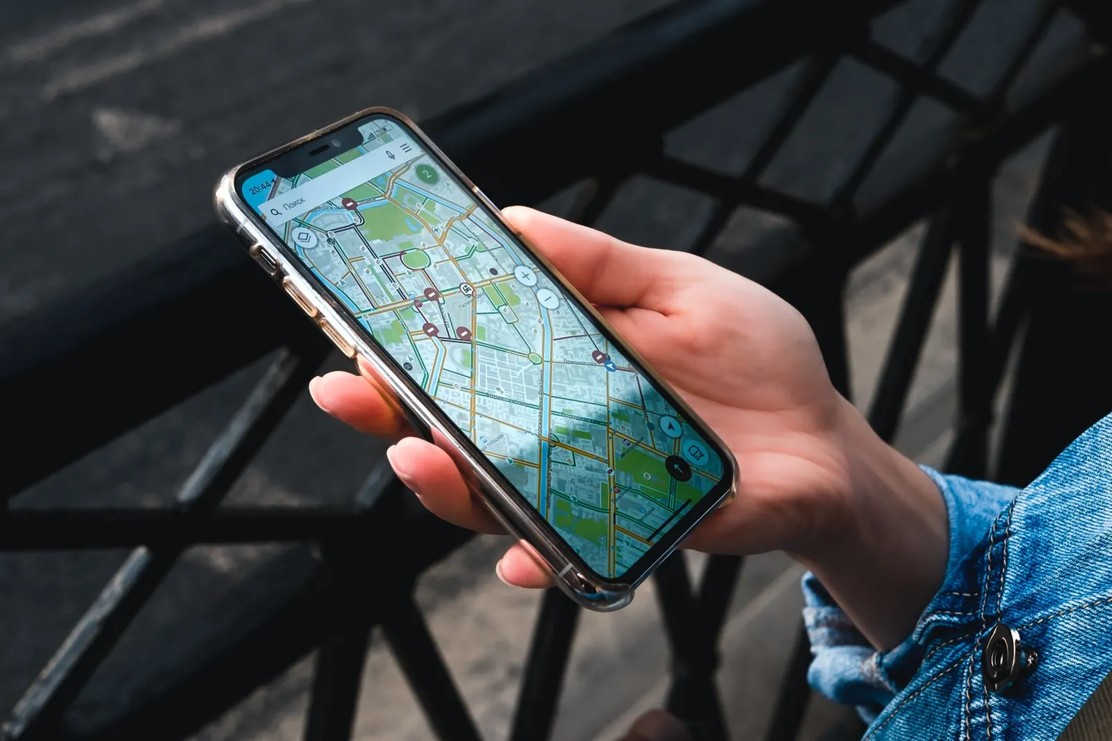 Een hand houdt een smartphone met een kaart op het scherm vast, naast een metalen hek