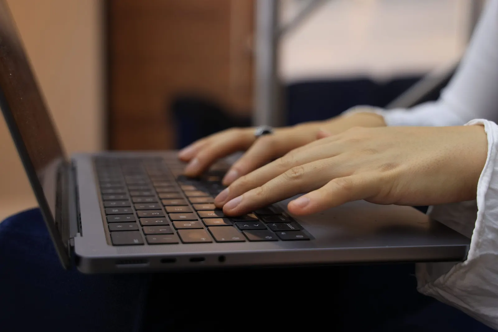 Twee handen typen op het toetsenbord van een grijze laptop aan een bureau