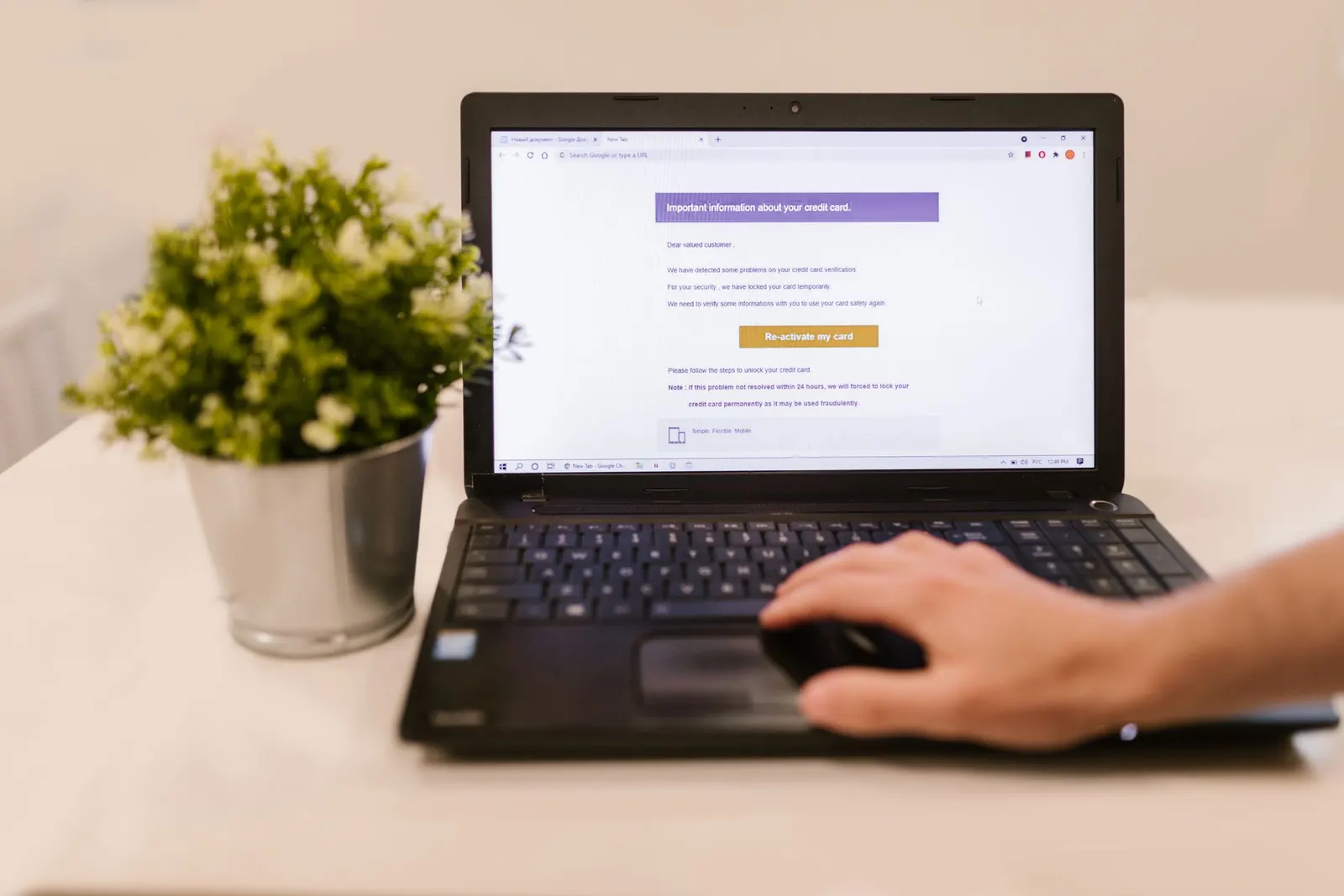 Iemand leest een e-mail op een laptop die op een wit bureau staat, naast een plantje in een metalen pot
