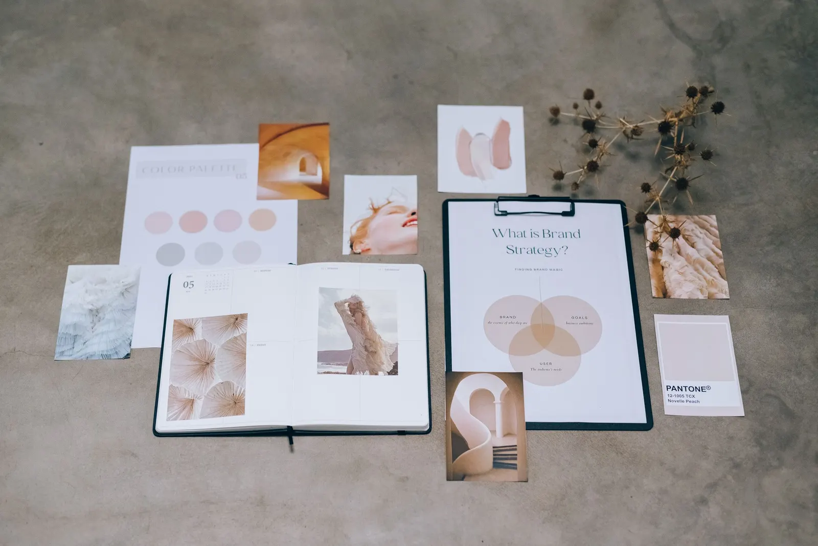 Bovenaanzicht van een betonnen tafel met kleurstalen, een notitieboek, moodboardbeelden en een klembord met een merkstrategie
