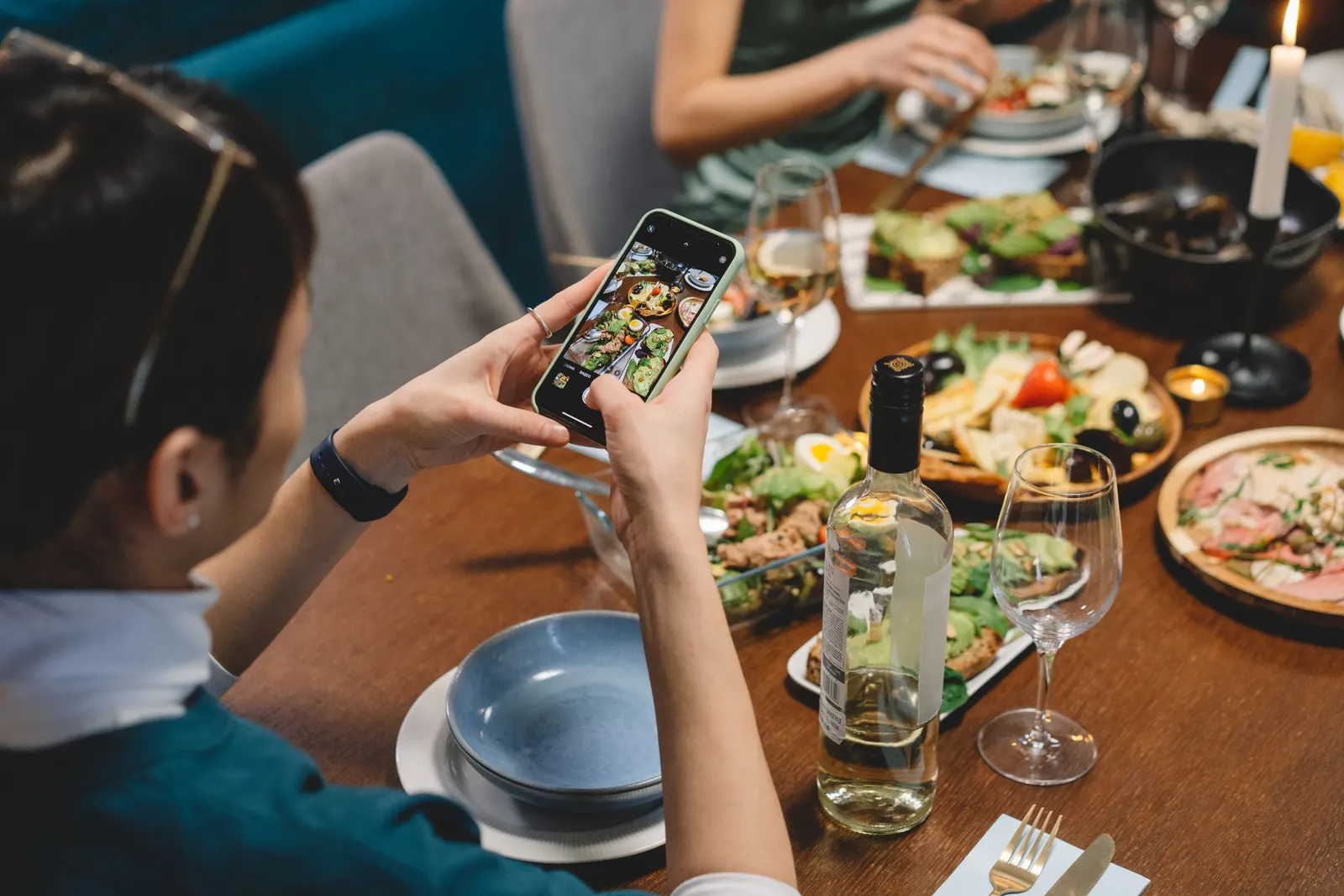 Een vrouw fotografeert met haar smartphone een tafel vol gerechten en wijnglazen in een restaurant