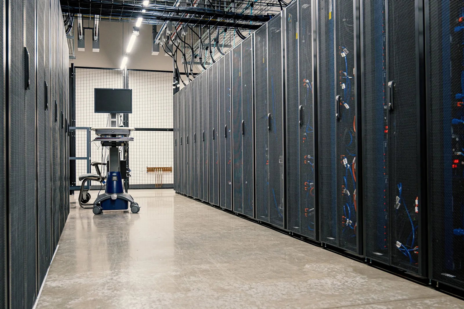 Een gang in een datacenter met rijen zwarte serverkasten en een werkstation op wieltjes
