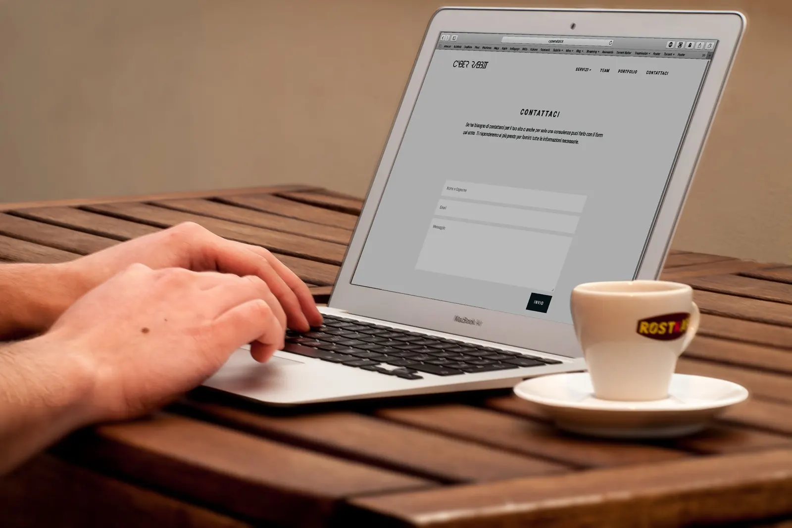 Handen typen op een laptop die een webpagina met een contactformulier toont, naast een kop koffie op een houten tafel