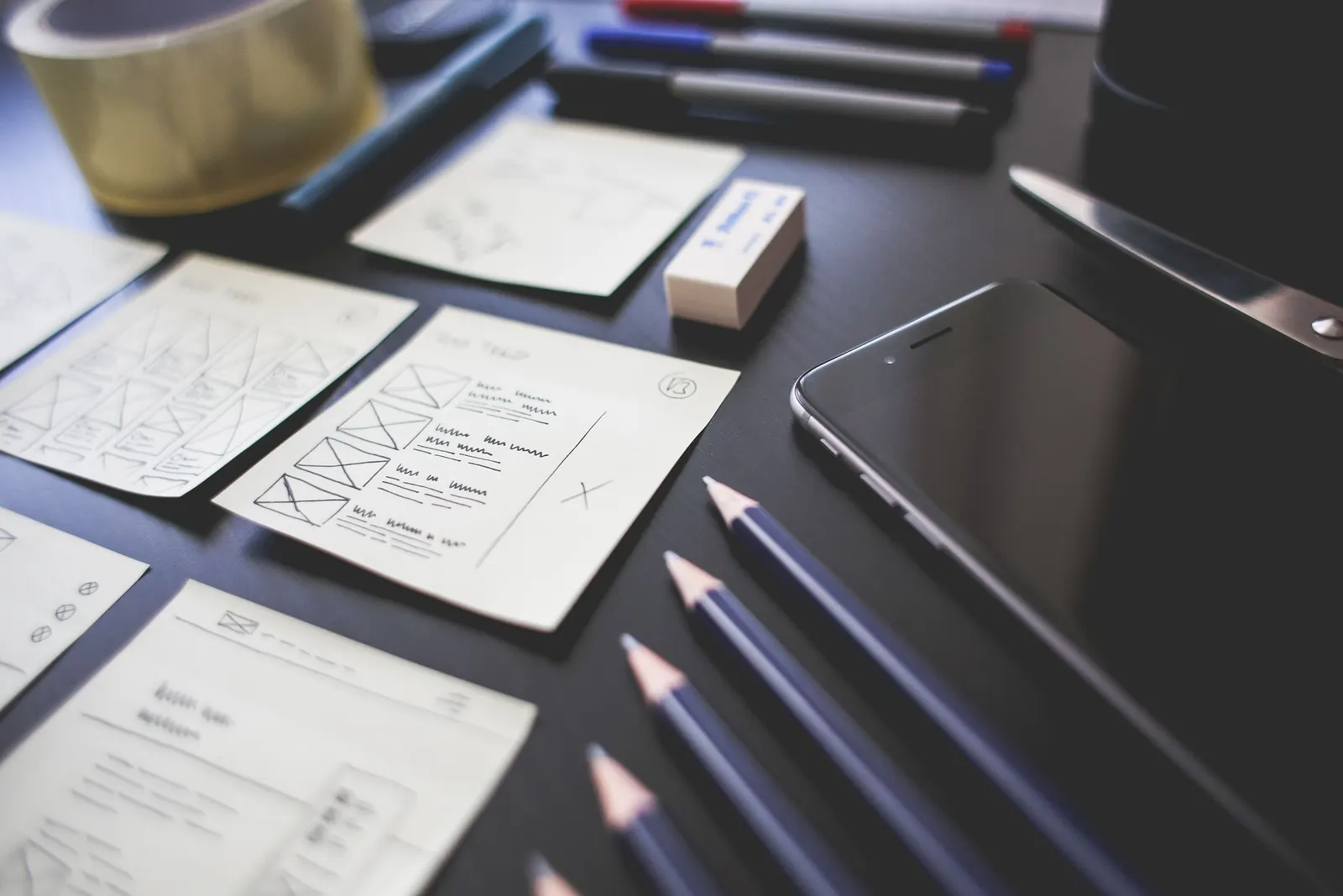 Een bureau met schetsen van schermontwerpen op papier, potloden en een smartphone
