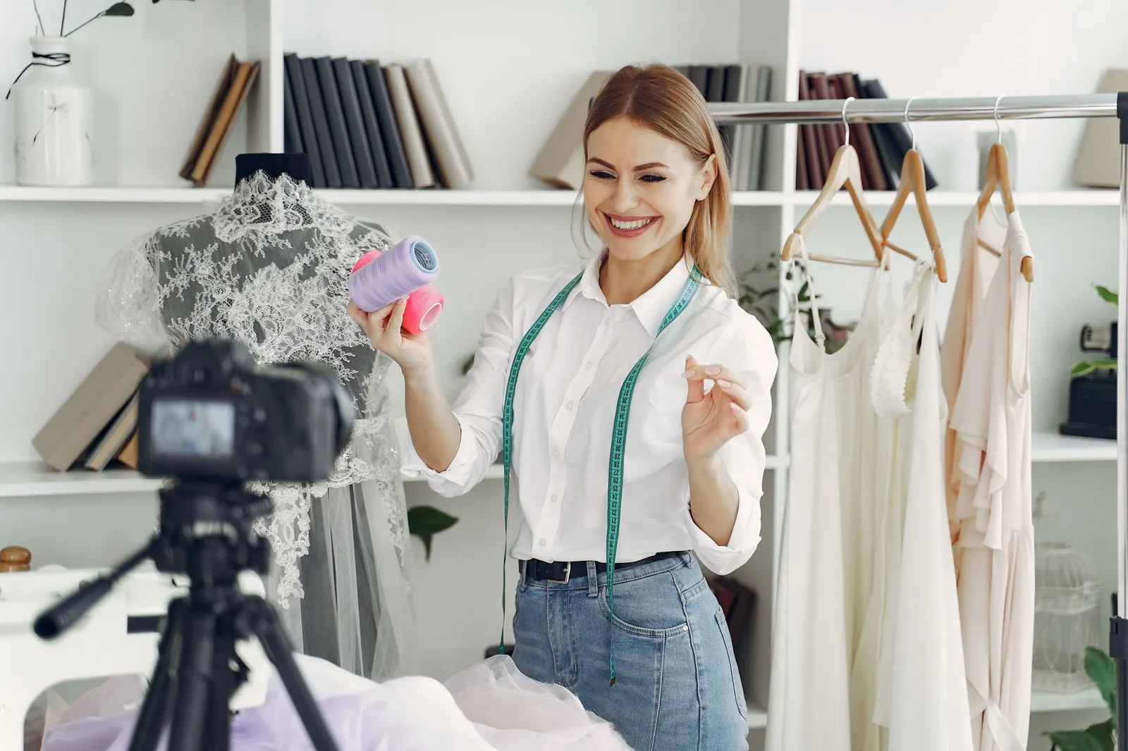 Uma empresária sorridente grava um vídeo no seu atelier com uma câmara num tripé