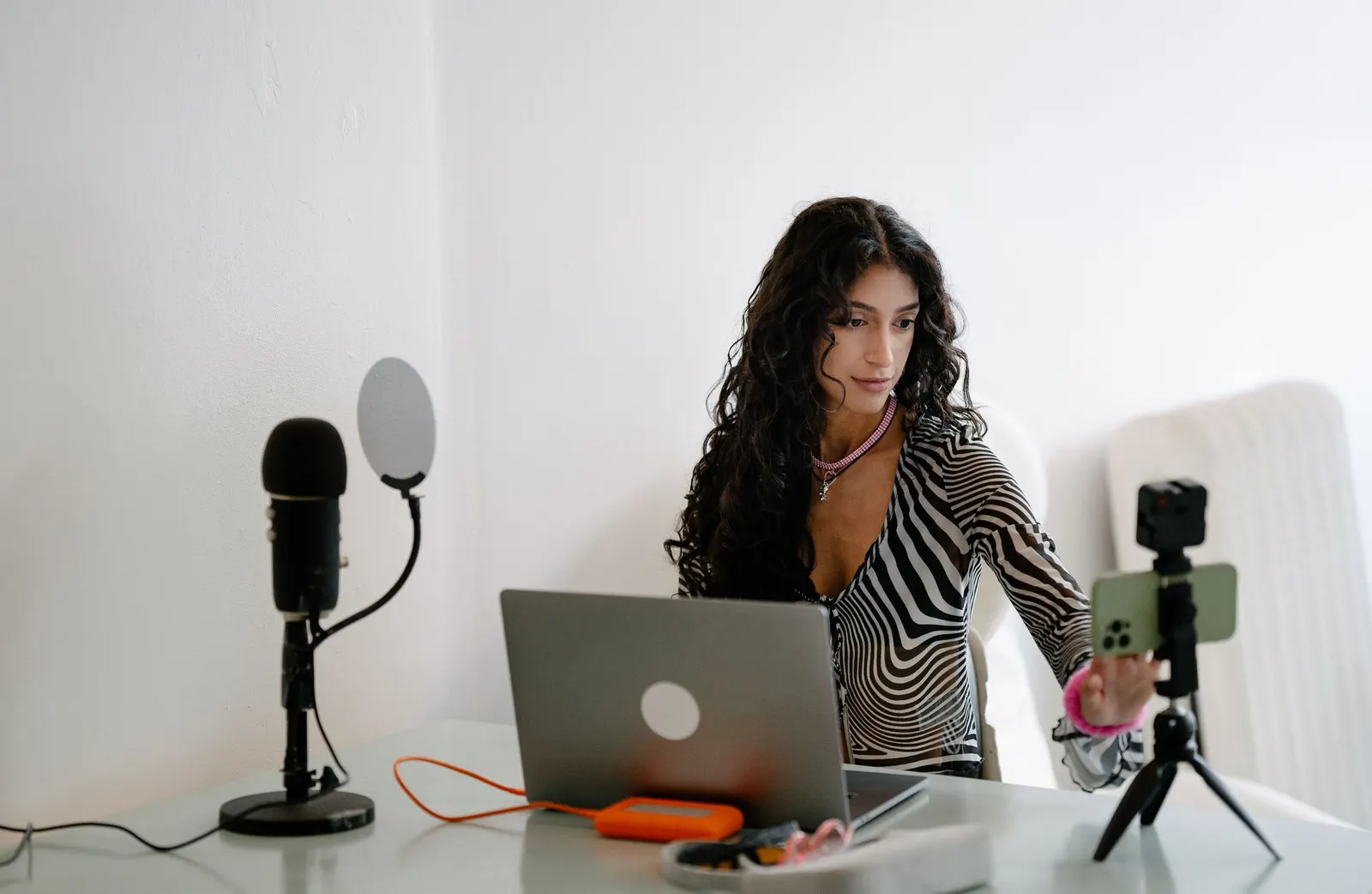 Vrouw achter een laptop met een microfoon en een smartphone op een statief, klaar om een video op te nemen