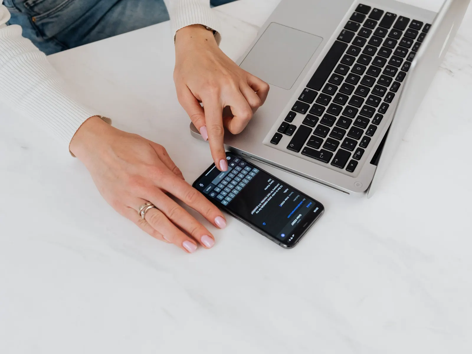 Iemand typt een vraag op een smartphone naast een laptop op een wit bureau