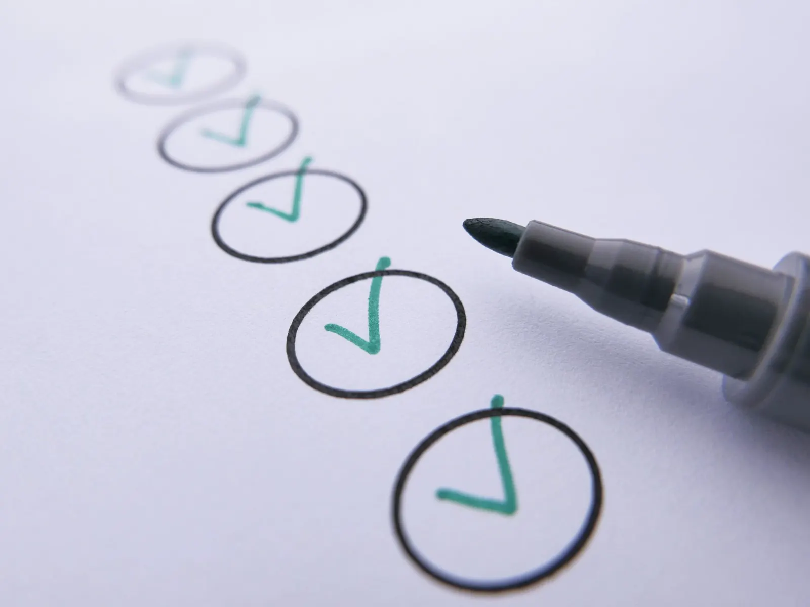 Een rij cirkels op wit papier wordt met een zwarte stift afgevinkt met groene vinkjes