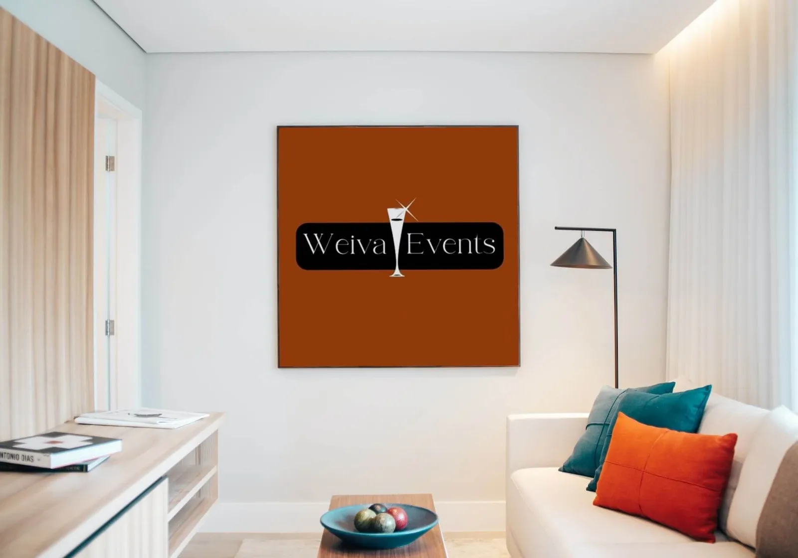 Het logo van Weiva Events op een oranje wand in een lichte woonkamer, naast een bank en een staande lamp