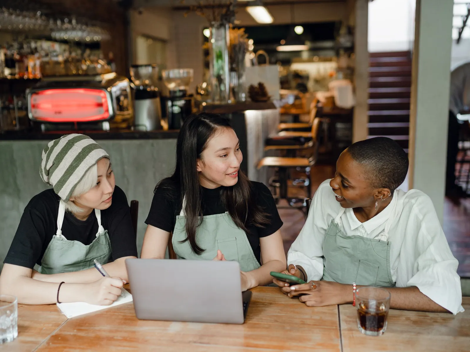 Drie medewerkers van een restaurant in schorten werken samen aan een laptop aan een houten tafel in het restaurant
