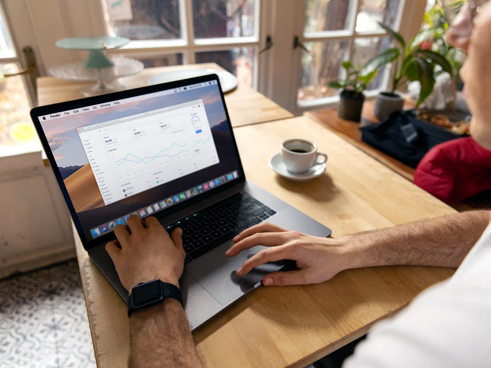 Iemand werkt op een laptop met grafieken van het websitebezoek, aan een houten tafel naast een kop koffie