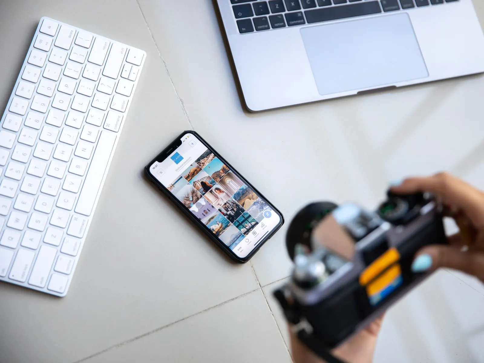 Iemand fotografeert boven een bureau met een laptop, een toetsenbord en een smartphone die een raster met berichten toont