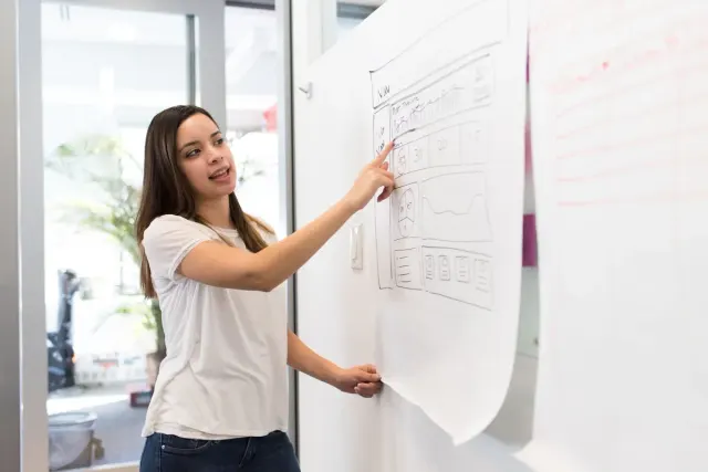 Een ontwerpster licht de schets van een website toe op een whiteboard