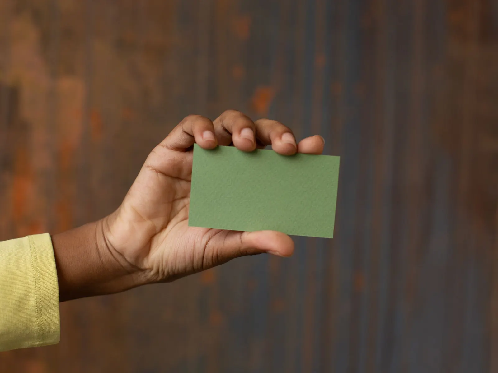 Een hand houdt een groen visitekaartje omhoog voor een donkere houten wand