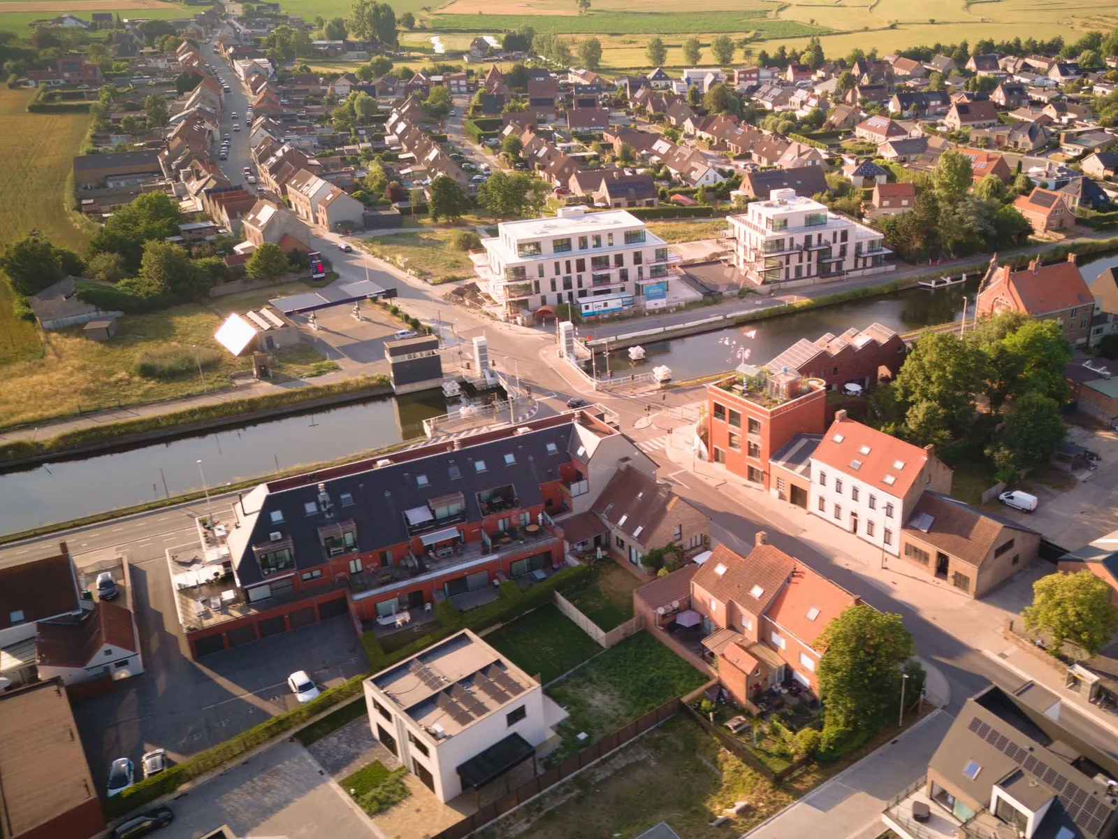 Luchtfoto van Oudenburg met woonwijken, een kanaal en velden tot aan de horizon